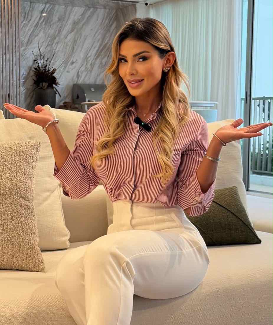 Fabia Fernandes sentada num sofá claro, de camisa listrada, com as mãos abertas